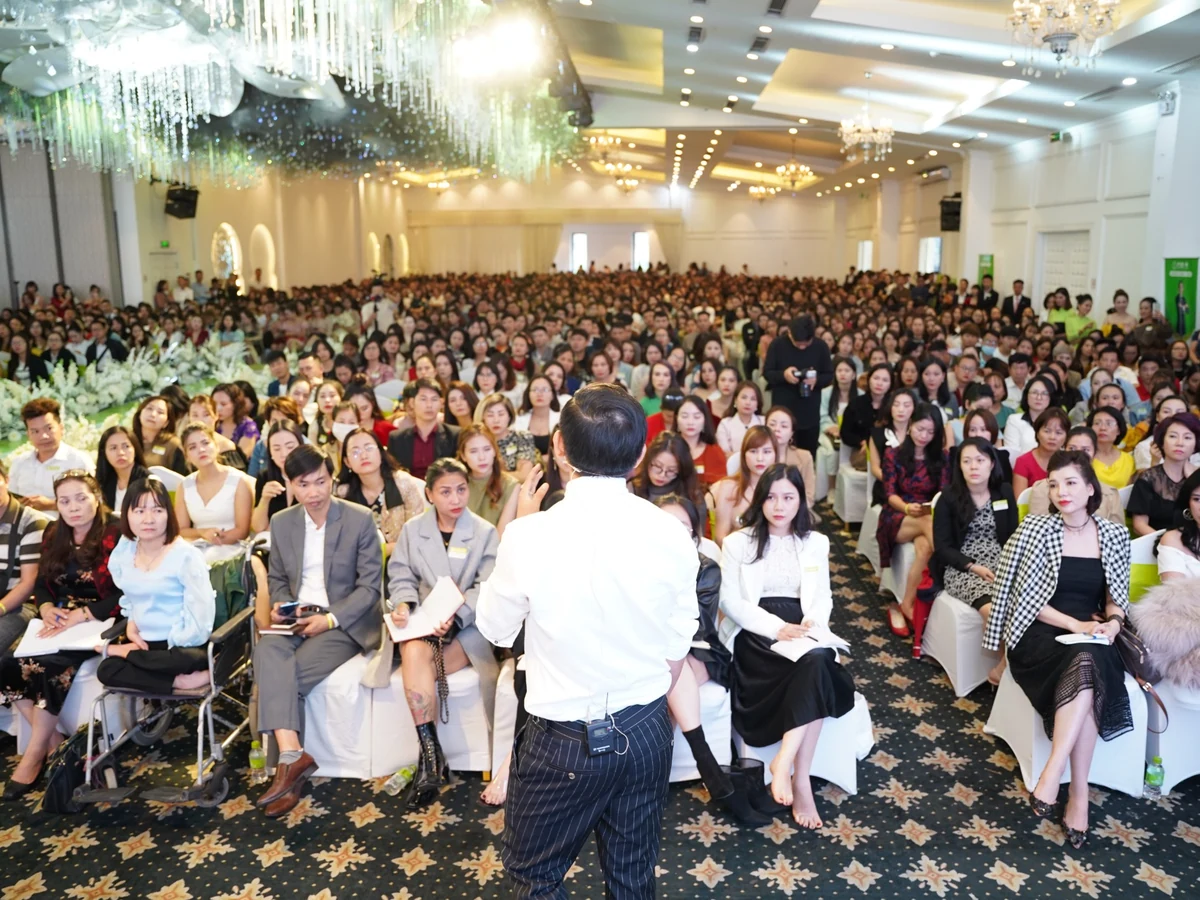 Diễn giả đứng trước hội trường đông người tham dự một buổi đào tạo.