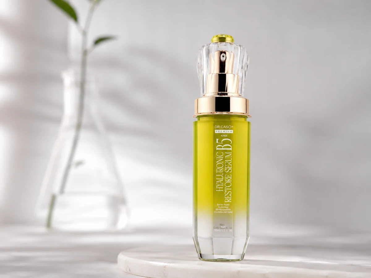 Chai Hyaluronic B5 Restore Serum trên bệ trắng, phía sau là tán lá mờ.