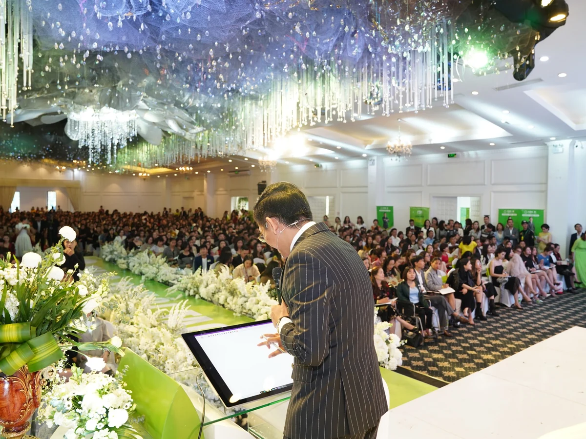 Diễn giả đứng bên bục thuyết trình, phía trước là khán phòng đông học viên.