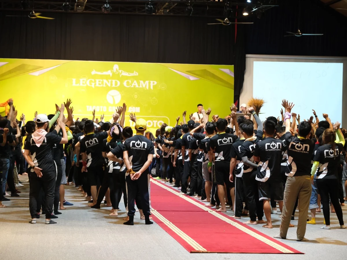 Nhóm thành viên áo tối màu tham gia hoạt động giơ tay trong hội trường Legend Camp.